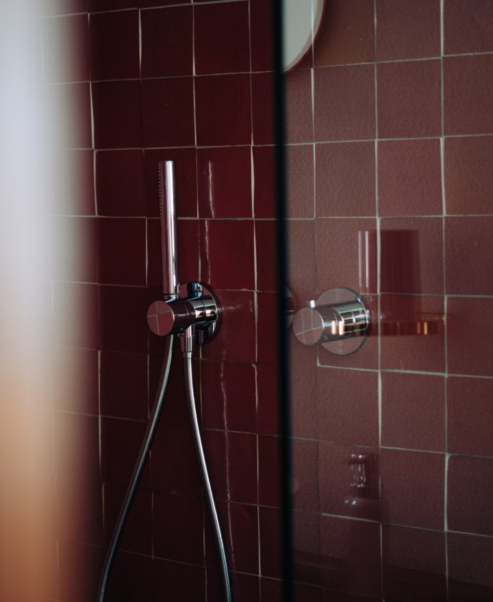 Hotelbadkamer met bordeauxrode zellige tegels en chromen doucheset, door cestsjoukje