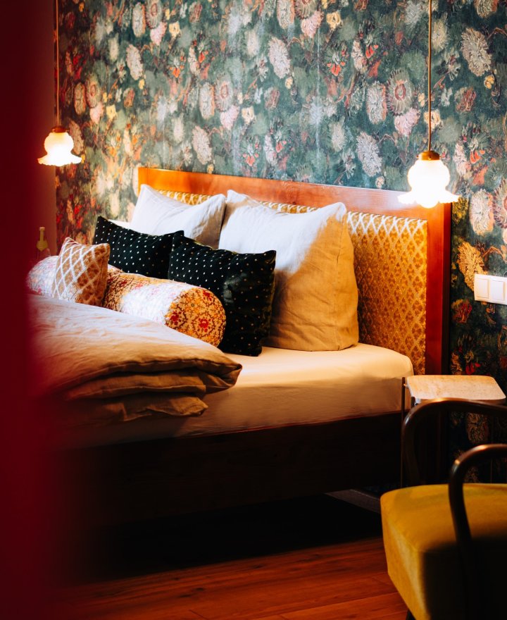Hotelkamer met bloemenbehang, houten hoofdbord in okergeel damast en gelaagde kussens in zwart, wit en oker, door cestsjoukje