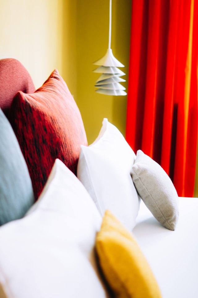 Hotel bed in rood, wit en oker tegen okergele wand en rood gordijn, door cestsjoukje