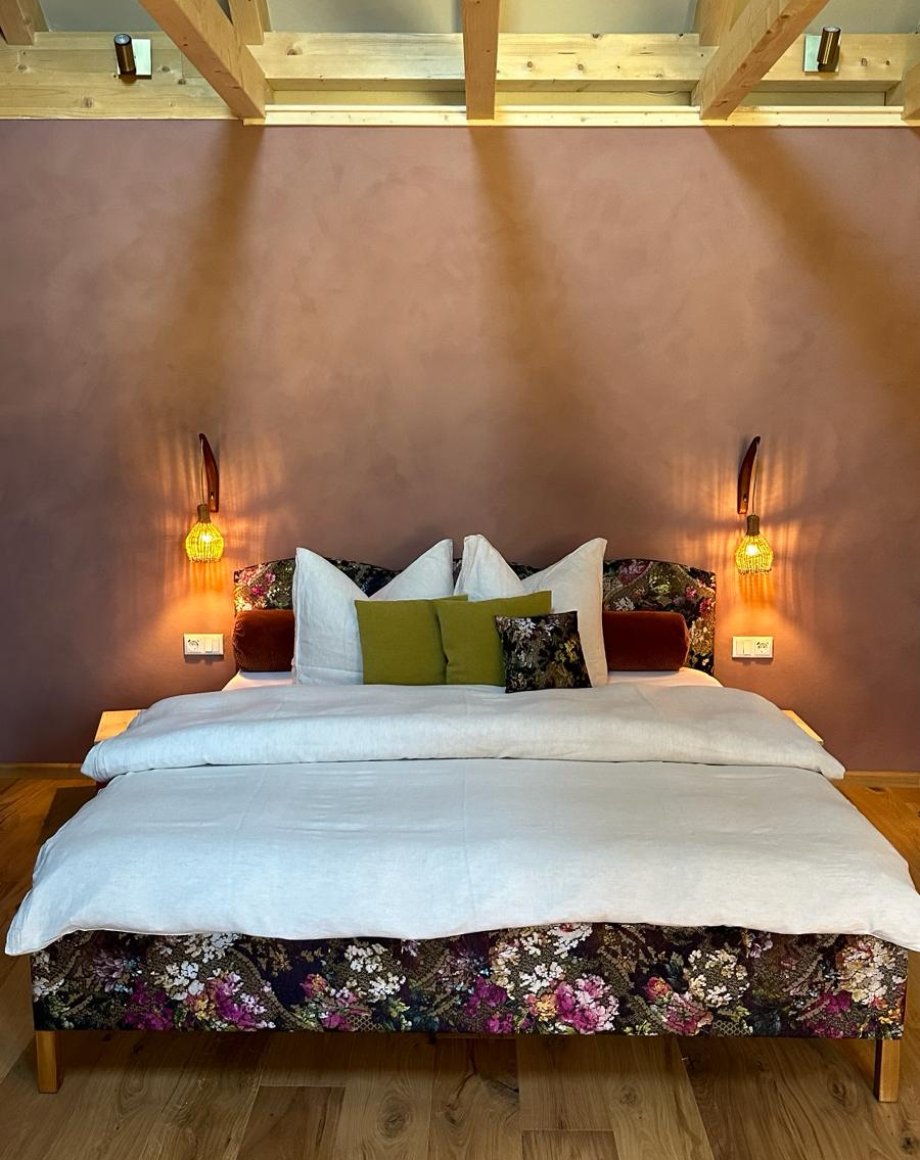 Hotelkamer met bloementextiel op het bed, warme wandlampjes en houten balkenplafond, door cestsjoukje