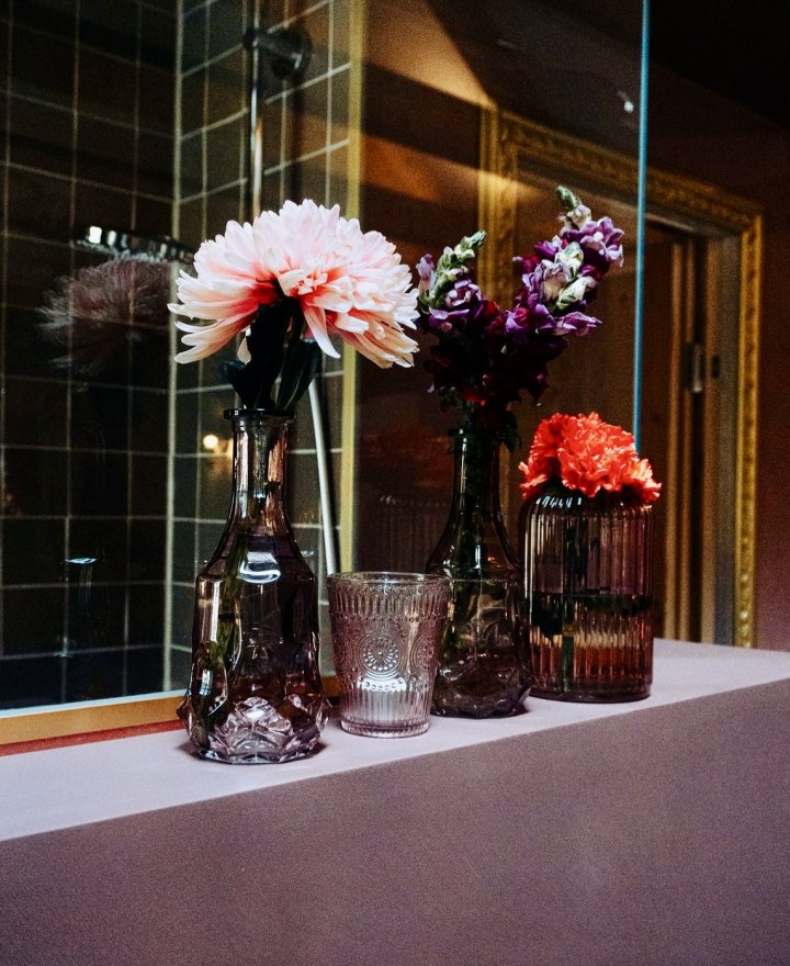 Hoteldouche met glazen vazen vol dahlia's en anjers voor een goudomlijste spiegelwand, hotelinterieur door cestsjoukje